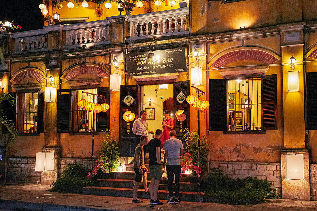  Menschen stehen vor dem in der Abenddämmerung beleuchteten Gebäude des Sakura-Restaurants. Antike Stadt Hoi An, Provinz Quang Nam, Vietnam. 