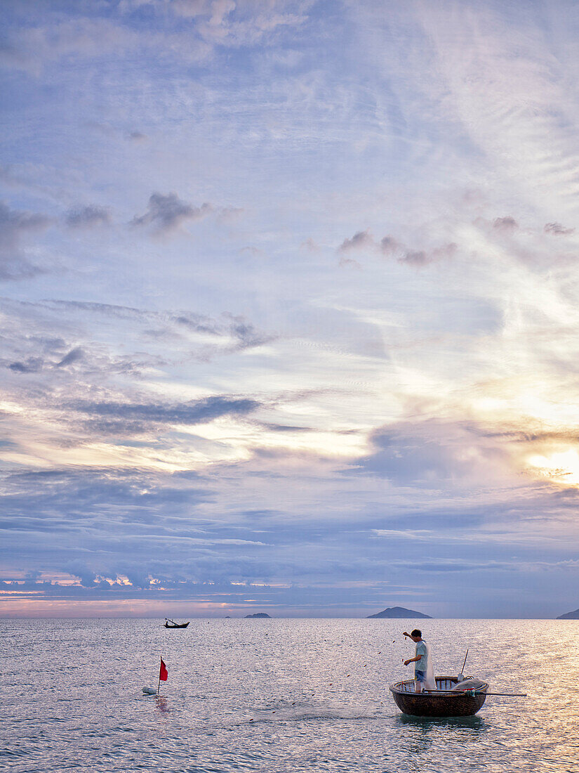 Vietnamese coracle fisherman pulls his net at sunrise. Hoi An, Quang Nam Province, Vietnam.