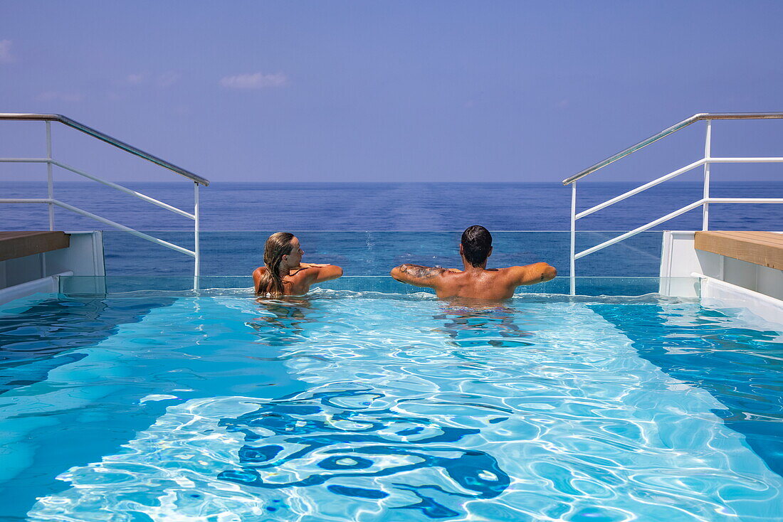  Woman and man relaxing on the edge of the infinity pool of the expedition cruise ship SH Diana (Swan Hellenic), at sea, near Saudi Arabia, Middle East 