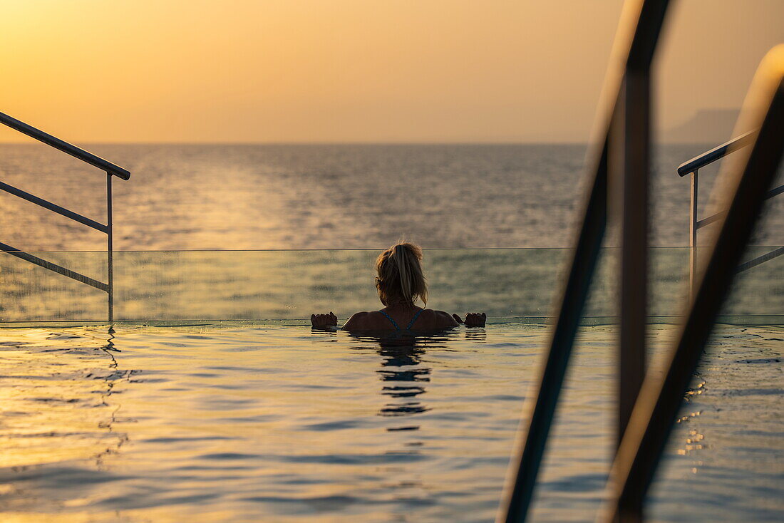  Silhouette of a woman relaxing on the edge of the infinity pool on the aft deck of the expedition cruise ship SH Diana (Swan Hellenic) at sunset, at sea, near Yemen, Middle East 