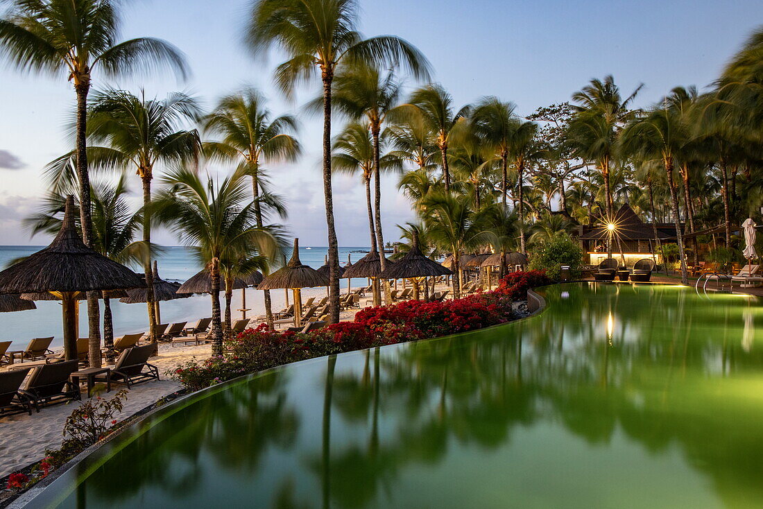 Swimmingpool und strohgedeckte Palapa-Sonnenschirme mit Kokospalmen im Royal Palms Beachcomber Luxury in der Abenddämmerung, Grand Baie, Rivière du Rempart, Mauritius, Indischer Ozean