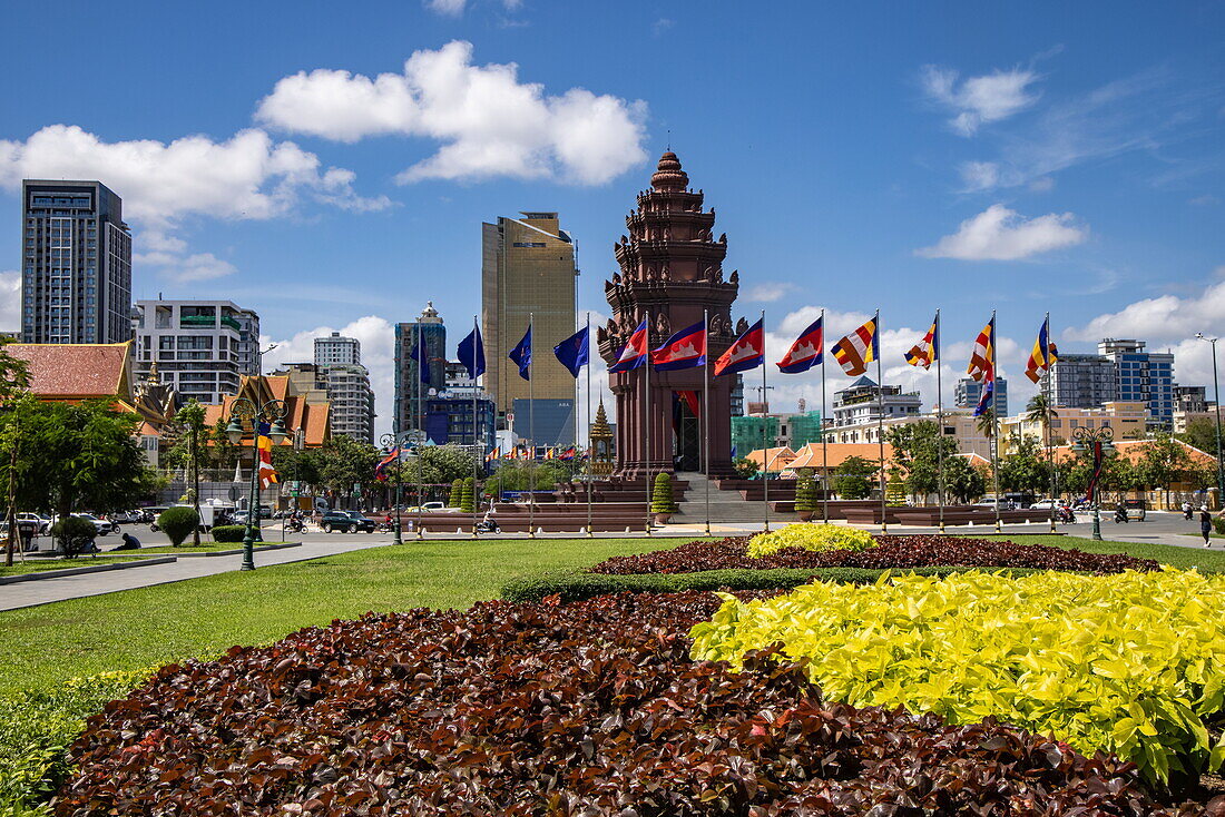 Flaggen am Unabhängigkeitsdenkmal im Stadtzentrum mit Skyline dahinter, Phnom Penh, Kambodscha, Asien