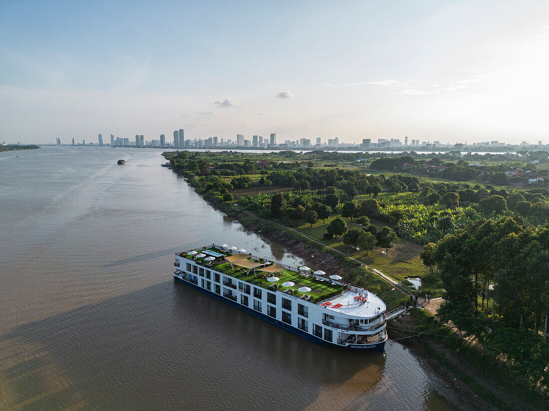  Aerial view of river cruise ship RV Mekong Discovery (Thurgau Travel) anchored next to “Silk Island” with the Phnom Penh skyline in the distance, Kaoh Oknha Tei, Khsach Kandal District, Kandal, Cambodia, Asia 