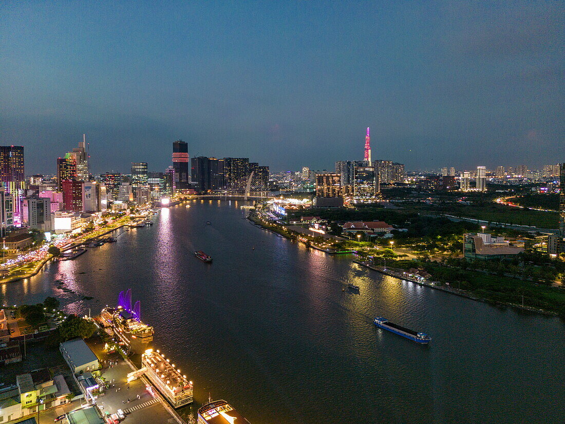  Aerial view of illuminated tourist tour boats along Saigon River with skyscrapers in District 1 city center and Landmark 81 tower in the distance at dusk, Quan 4, Ho Chi Minh City, Vietnam, Asia 