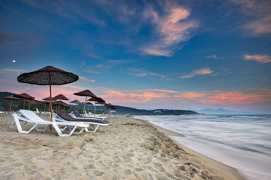 Sunbeds under parasols on the Pamucak Beach at dusk. Izmir Province, Turkey.