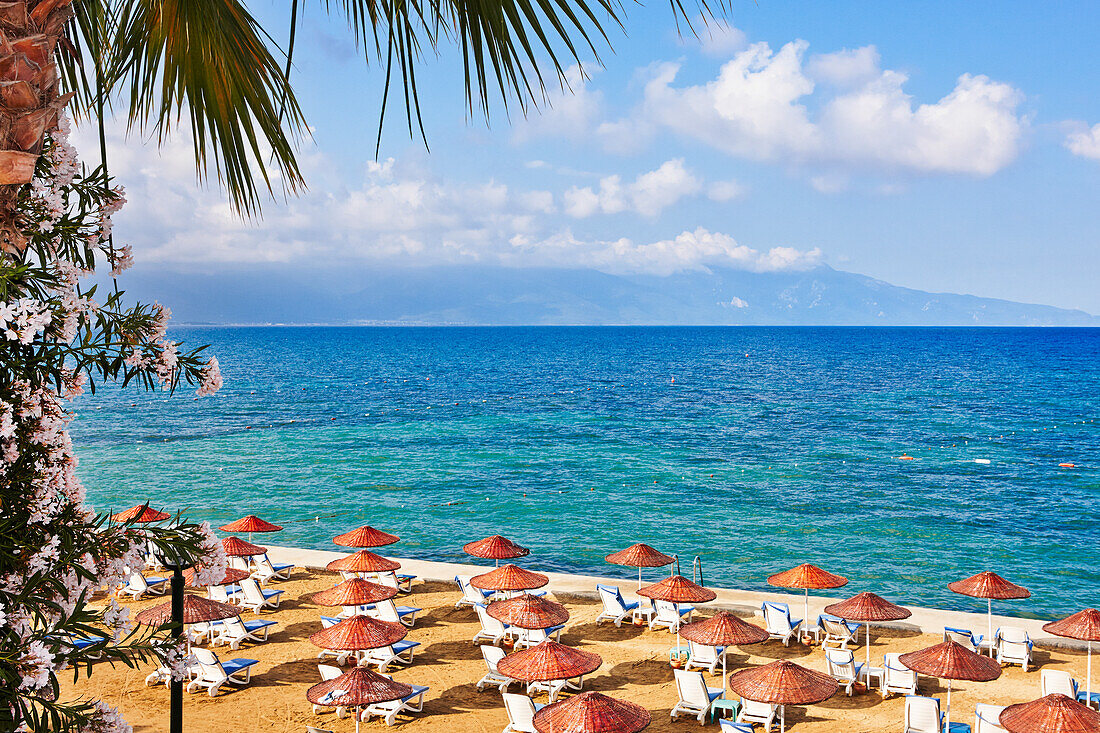 Sonnenliegen und Sonnenschirme an einem Sandstrand in Kusadasi, einem großen Ferienort an der Ägäis in der türkischen Provinz Aydin, Türkei