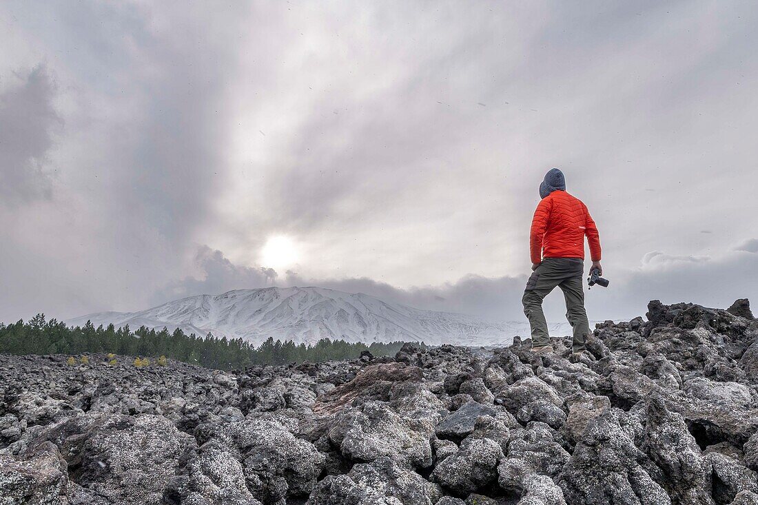  Man with camera standing on large lava field of Mount Etna with view of summit crater, UNESCO World Heritage Volcano, Stratocaster Volcano, Etna, Italy, Sicily\n 