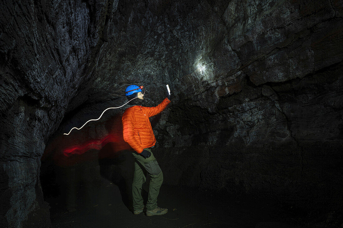  Man with helmet and flashlight stands inside a lava tunnel of Etna and studies the rock and the lava, lava tube, lava, protective equipment, lava equipment, cave, UNESCO World Heritage volcano, stratovolcano, Etna, Etna, Italy, Sicily,\n 