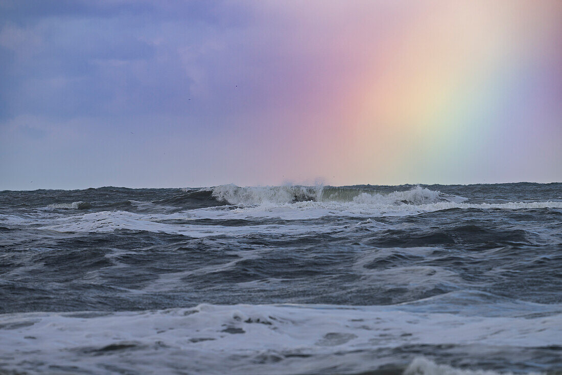 Ocean waves under a cloudy sky with a vibrant rainbow.