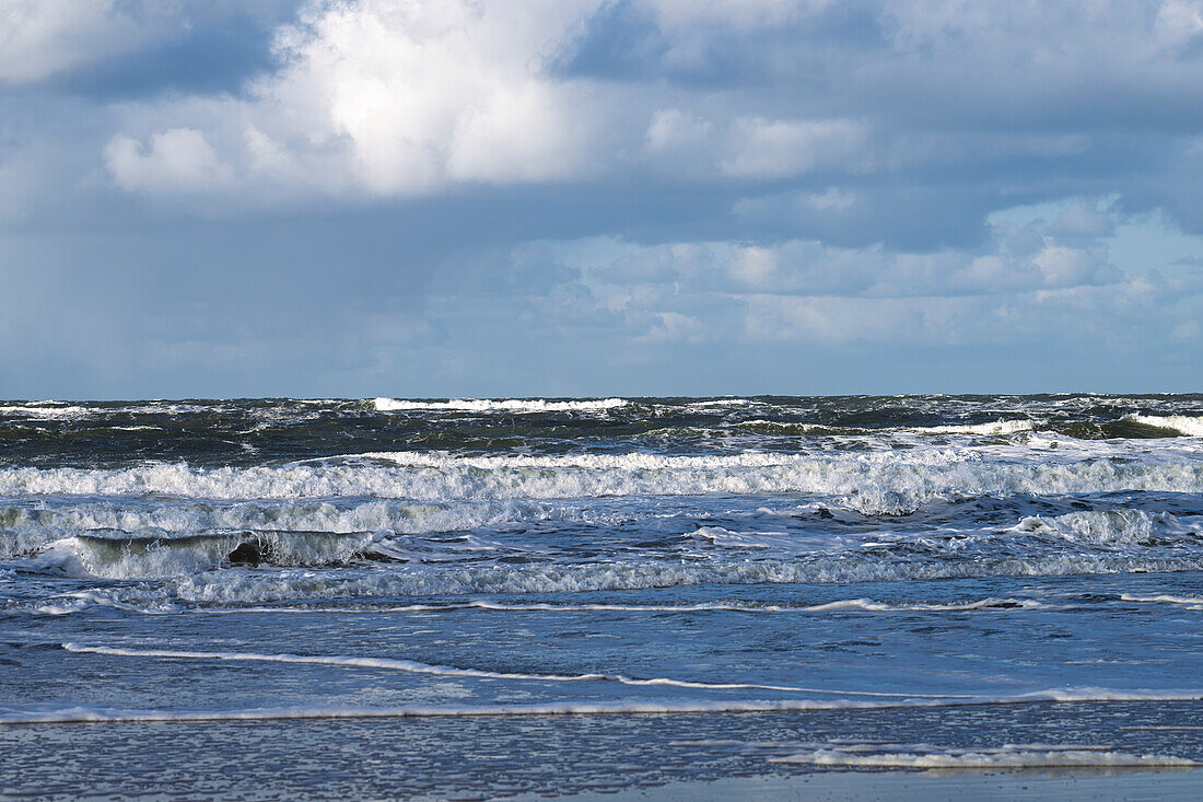 A scenic view of a turbulent ocean with waves crashing under a cloudy sky.