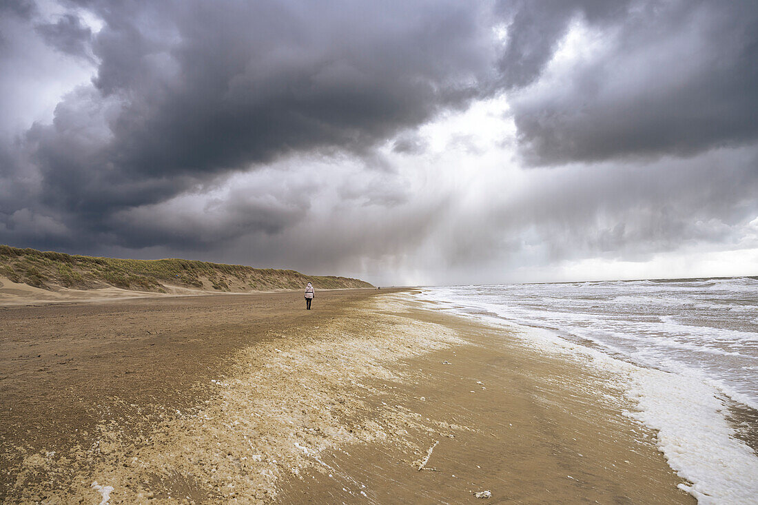 Dunkle Sturmwolken und Sonnenstrahlen am Strand vor dem aufgewühltem Meer, Westfriesische Insel Texel, Nordsee, Provinz Nordholland, Niederlande