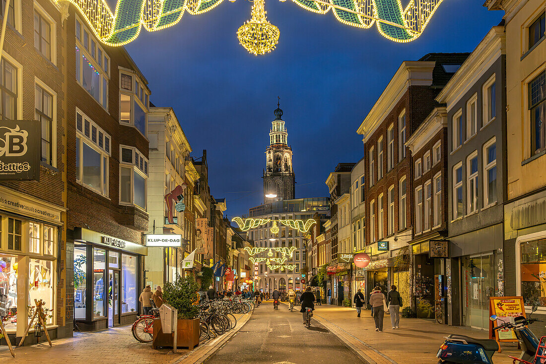 Einkaufsstrasse Oosterstraat und der Kirchturm Martinitoren oder Martiniturm der Martinikerk oder Martinikirche in der Abenddämmerung, Groningen, Niederlande