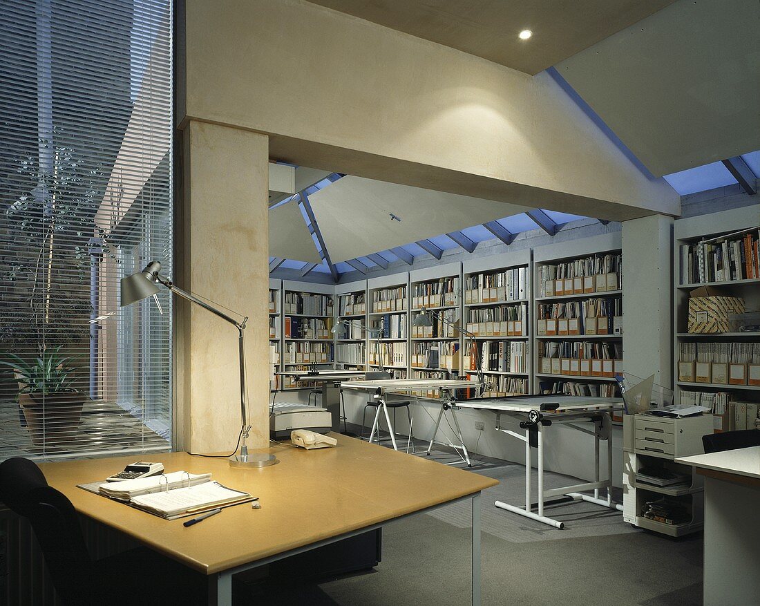 Architekturbüro mit beleuchtetem Tisch und Zeichentischen vor Einbauregal