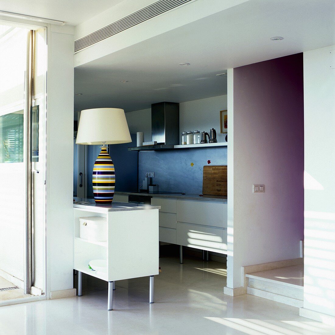 A living room with an open-plan kitchen and white cupboards