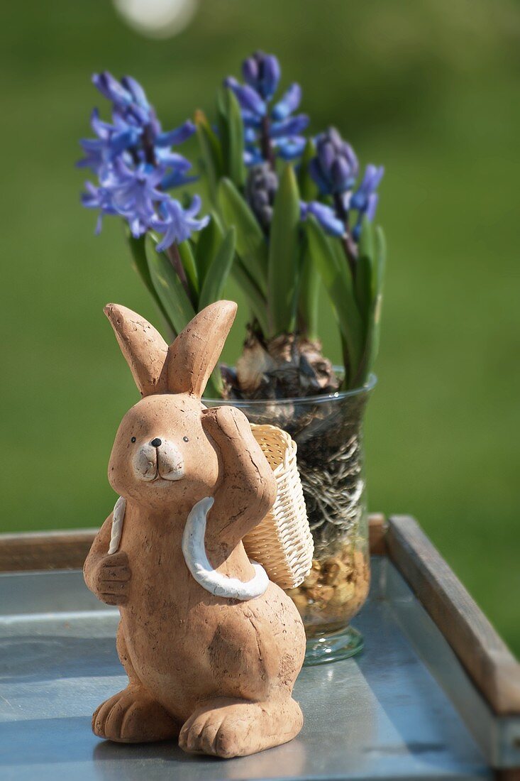 A clay rabbit figure in front of purple hyacinths in a glass