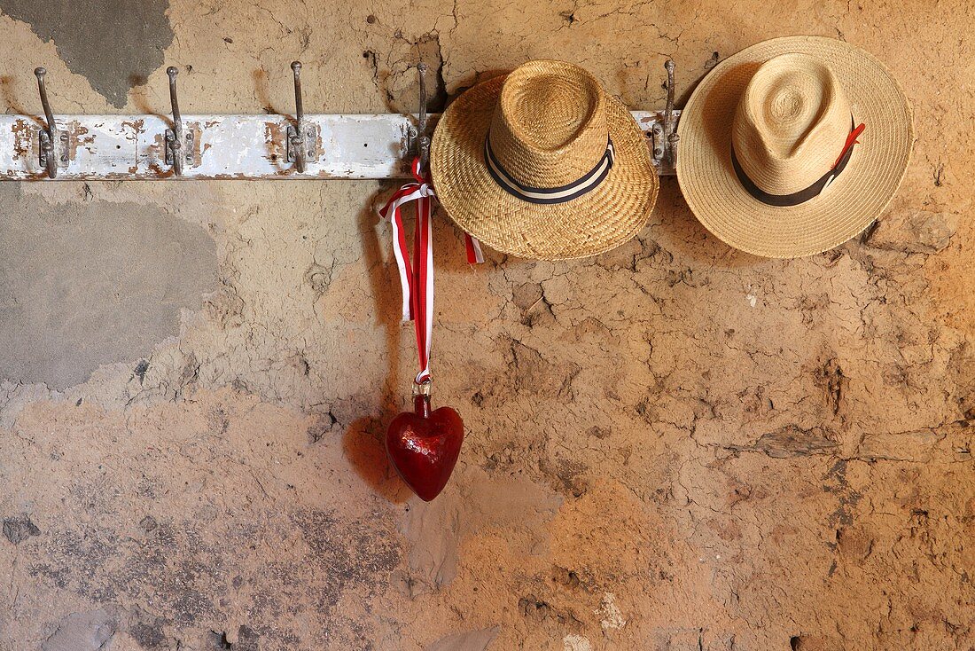 Straw hats and a glass heart on an old row of hooks