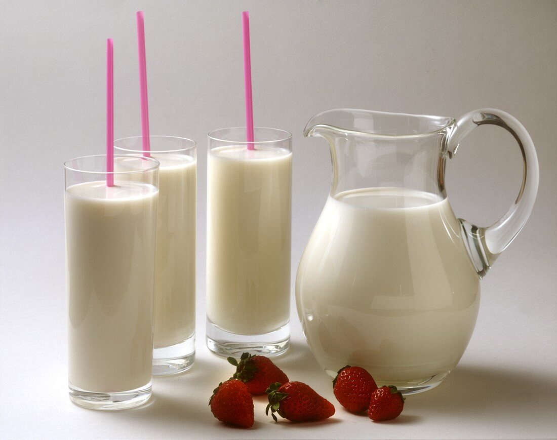 Drei Gläser Milch mit Strohhalm; Milchkrug; einige Erdbeeren