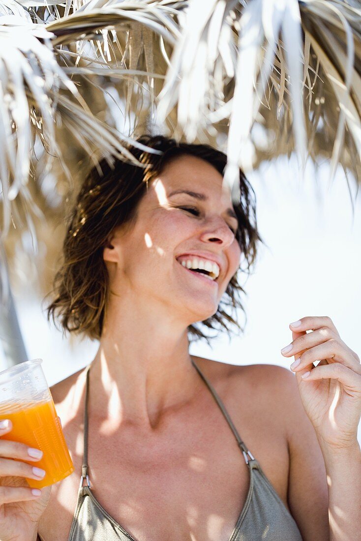 Woman with orange juice under a straw sunshade