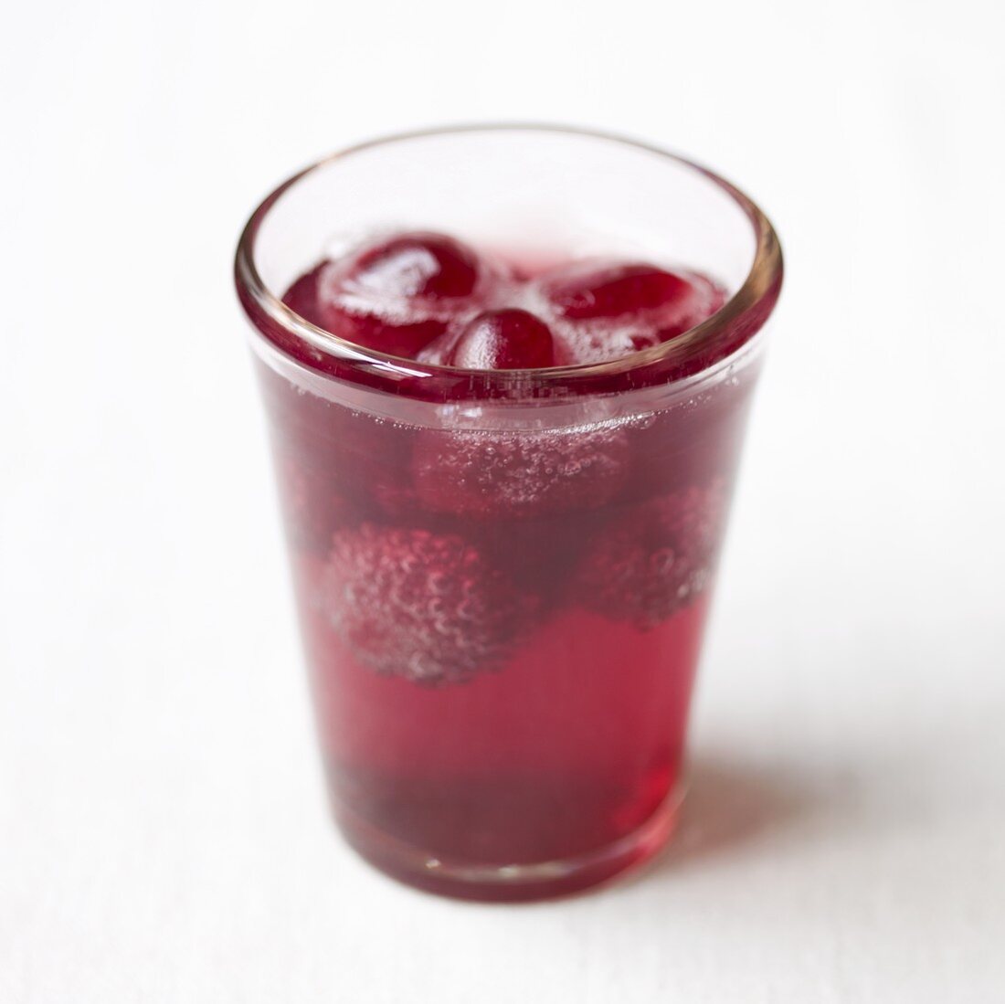 A glass of red lemonade with raspberries and cherries