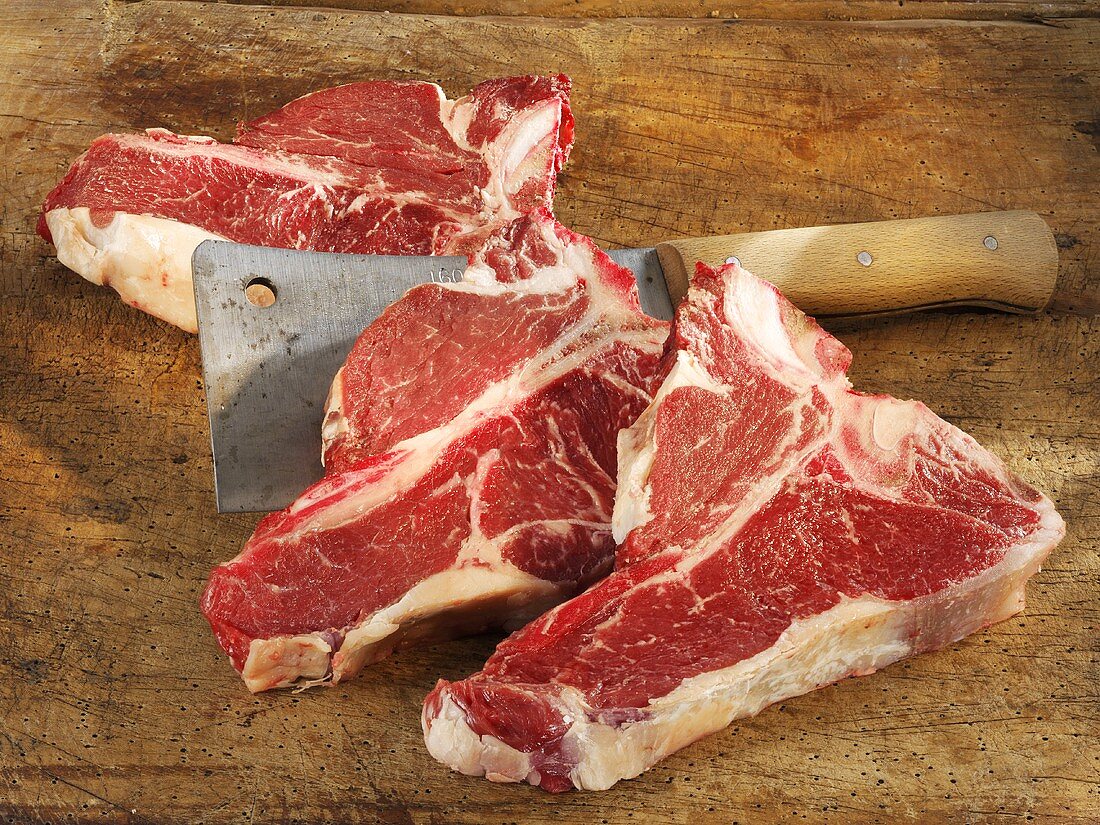 Raw Porterhouse steaks with cleaver on wooden background
