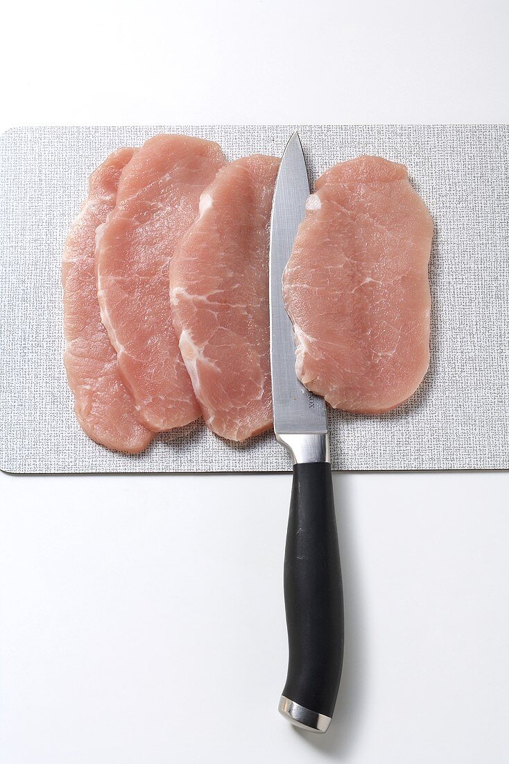 Four pork escalopes with knife on board