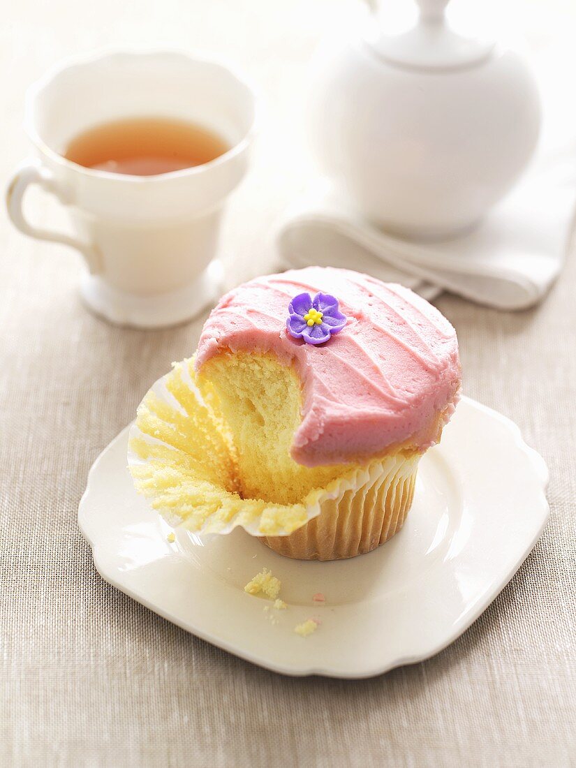 Partly-eaten cupcake with buttercream & sugar flower, tea
