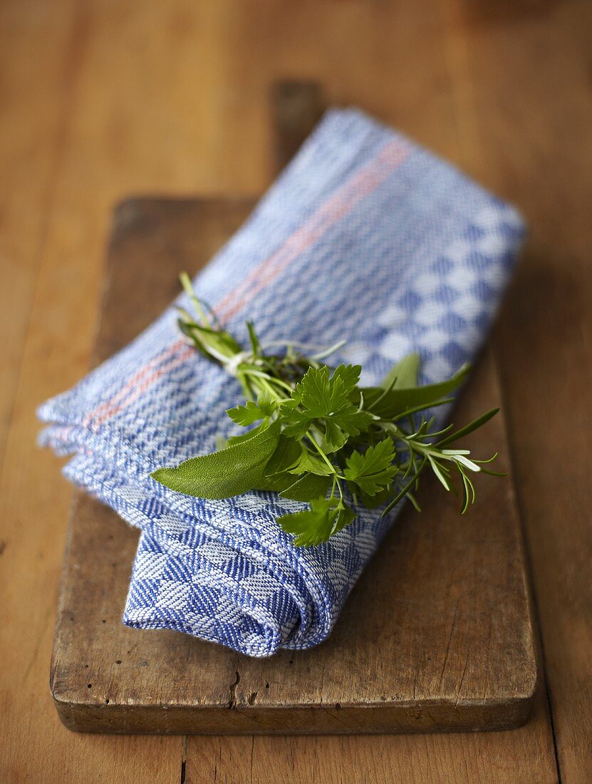 A small bouquet of herbs on a kitchen towel and a wooden board