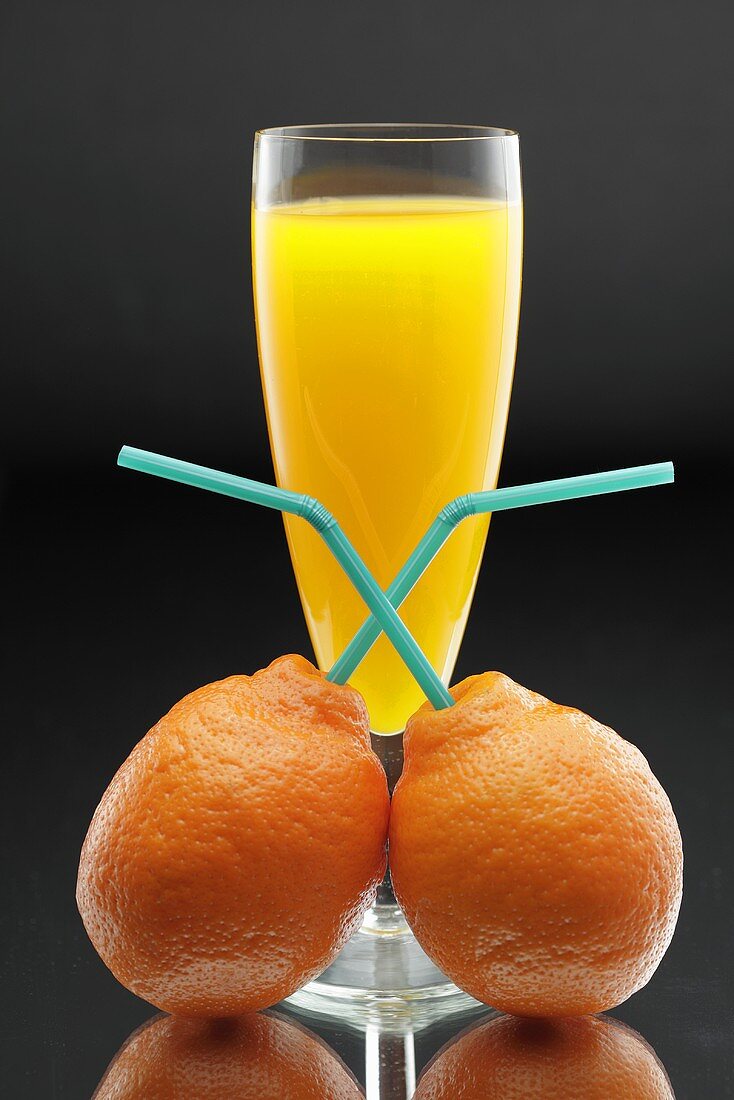 Tangerines with straws in front of a glass of juice