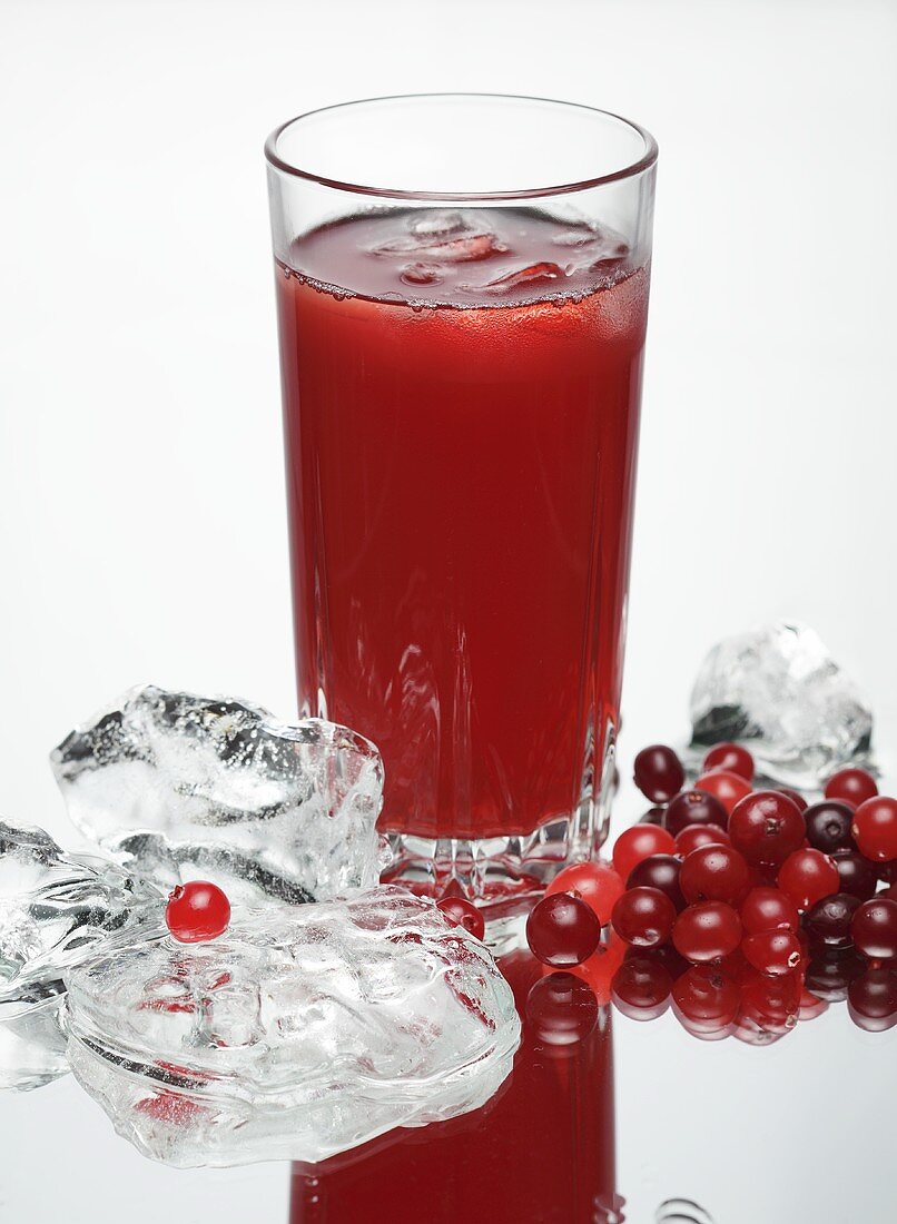 A glass of cranberry juice, fresh cranberries and ice cubes