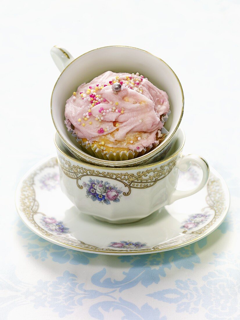 A cupcake with pink cream and sugar balls in a cup
