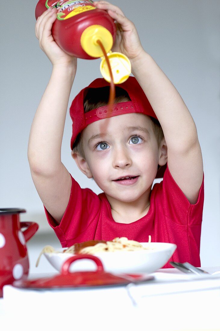 Kleiner Junge spritzt Ketchup auf Spaghetti