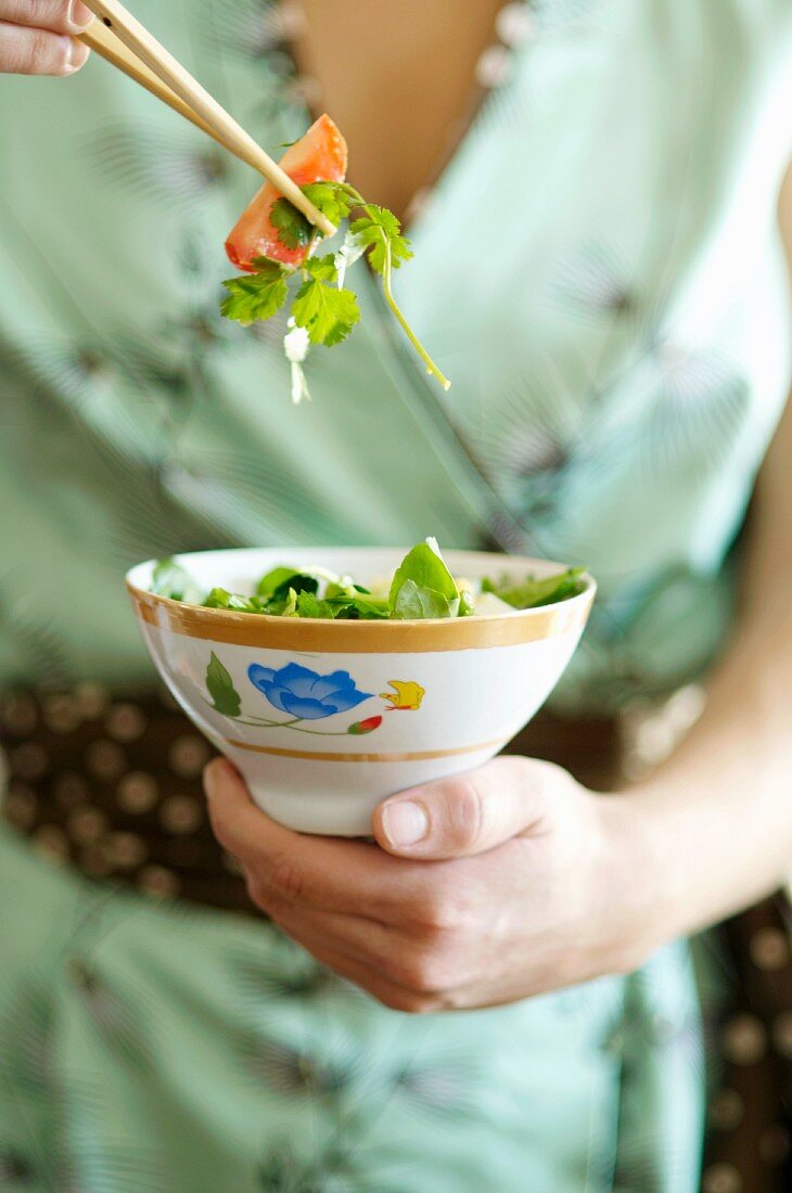 Hand hält Schälchen mit asiatischem Salat
