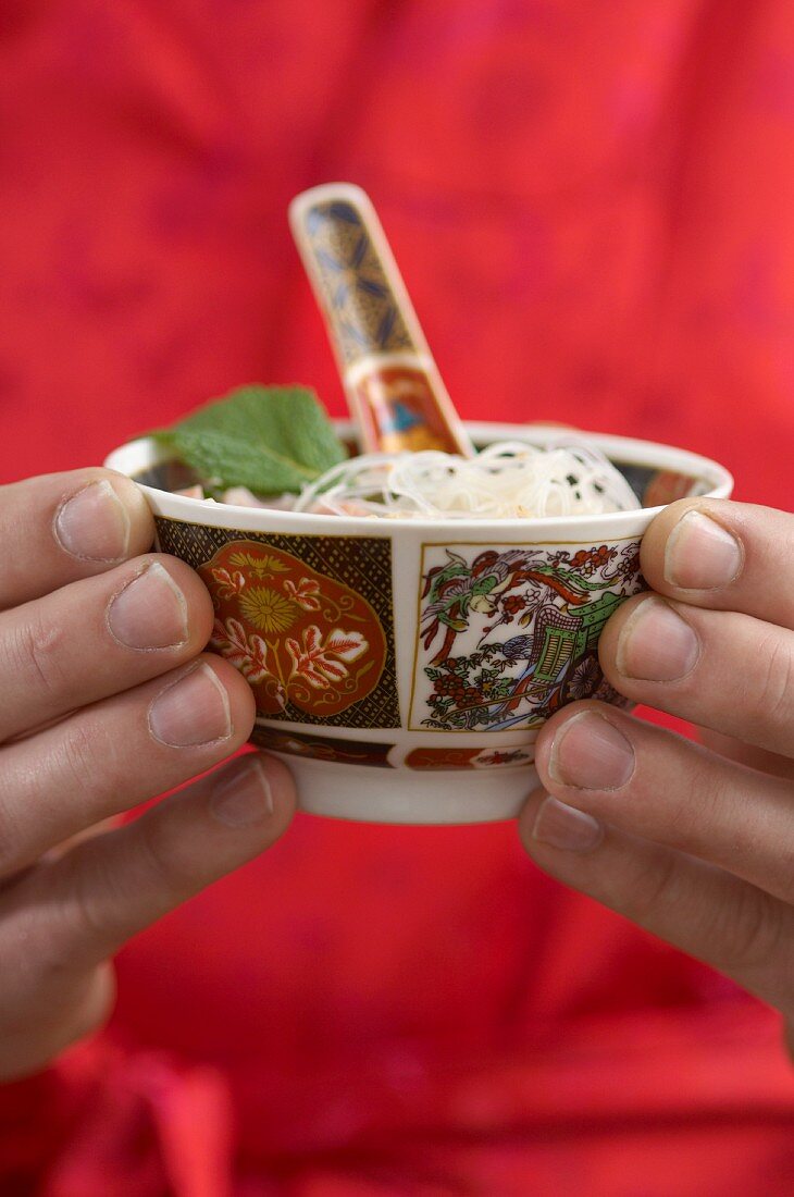 Hands holding a bowl of glass noodles