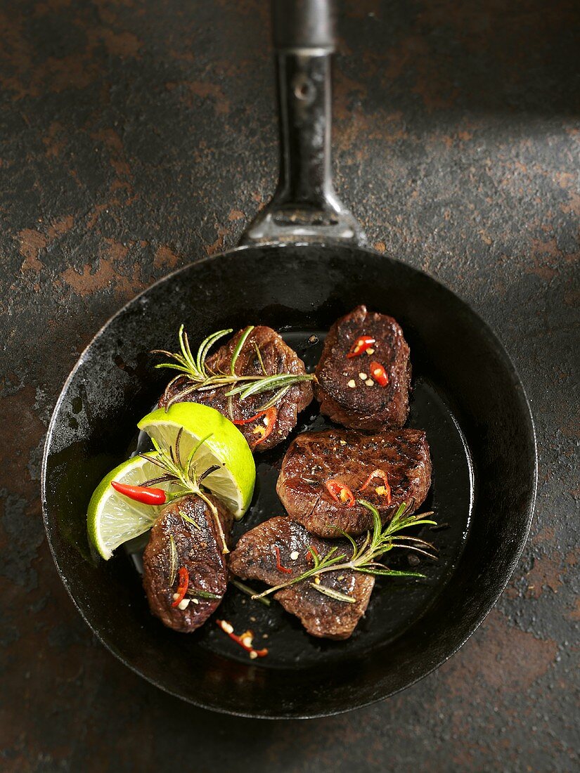 Känguruhsteaks mit Chilischoten, Limetten und Rosmarin in Pfanne