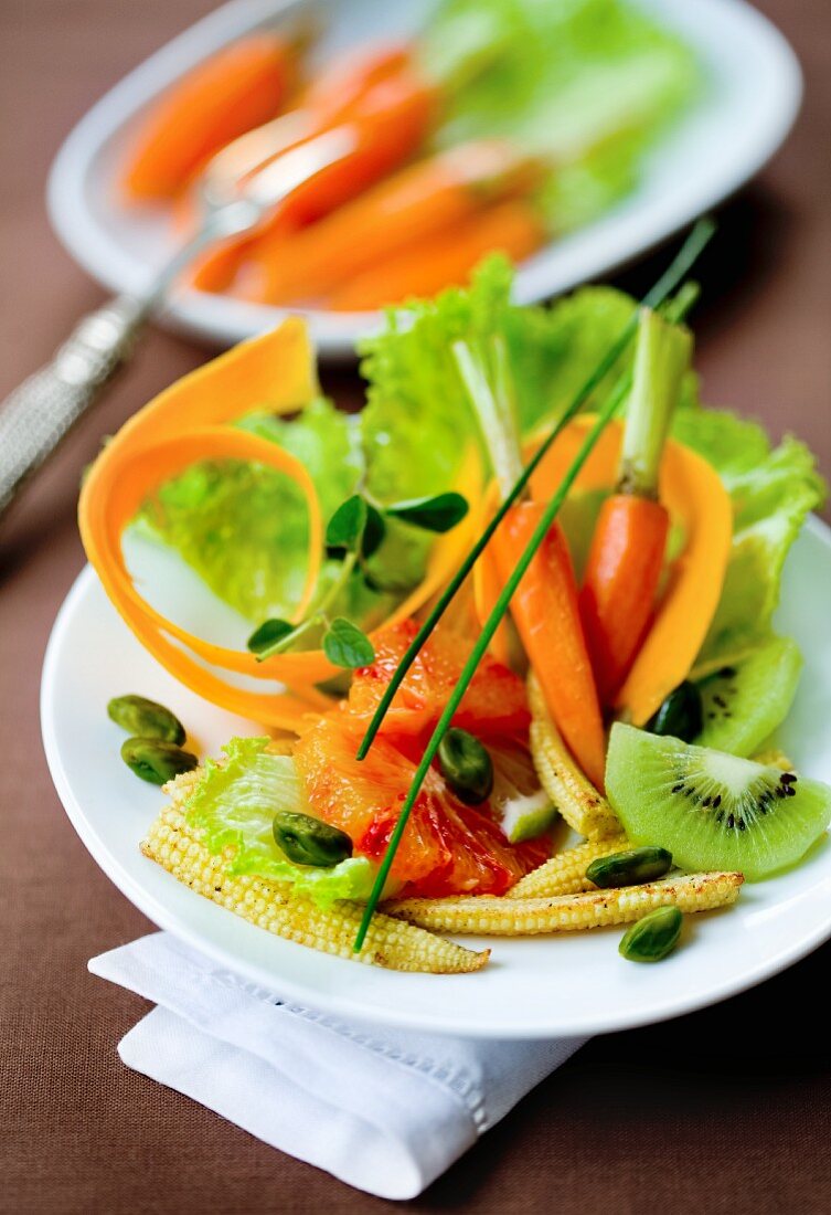 A mixed salad with carrots, baby corn cobs and kiwi