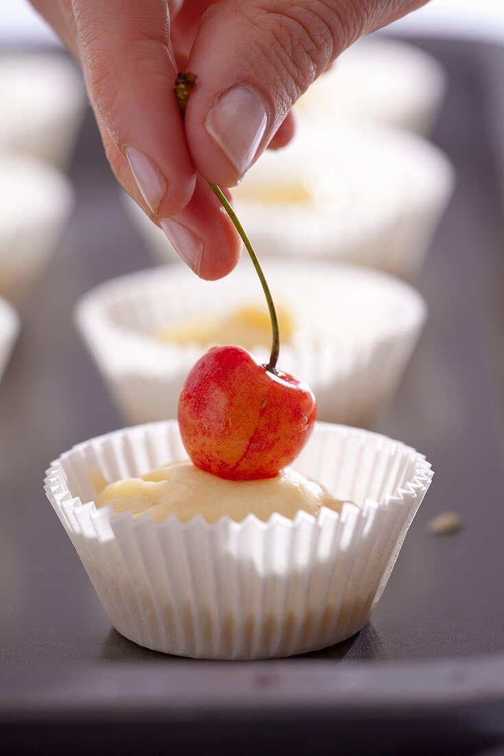 A hand placing a cherry on an unbaked muffin