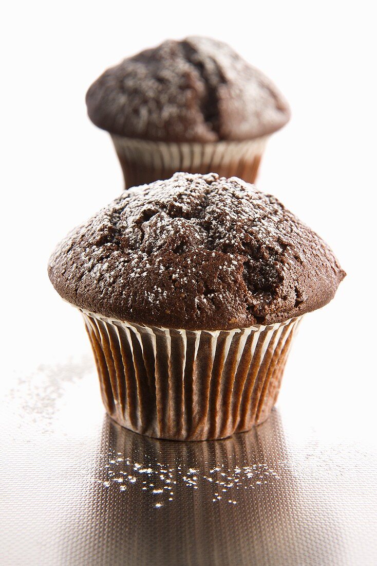 Two chocolate muffins with icing sugar