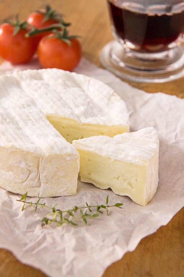 Camembert, sliced, on paper with tomatoes and a glass of red wine