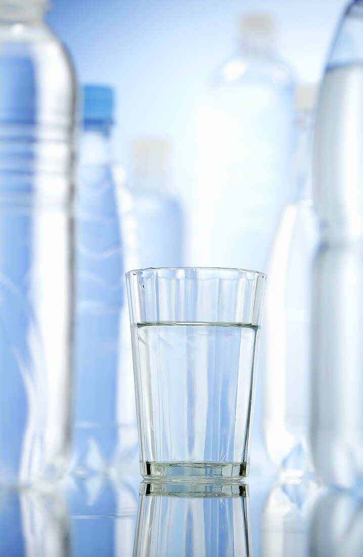 A glass of water between bottles of water