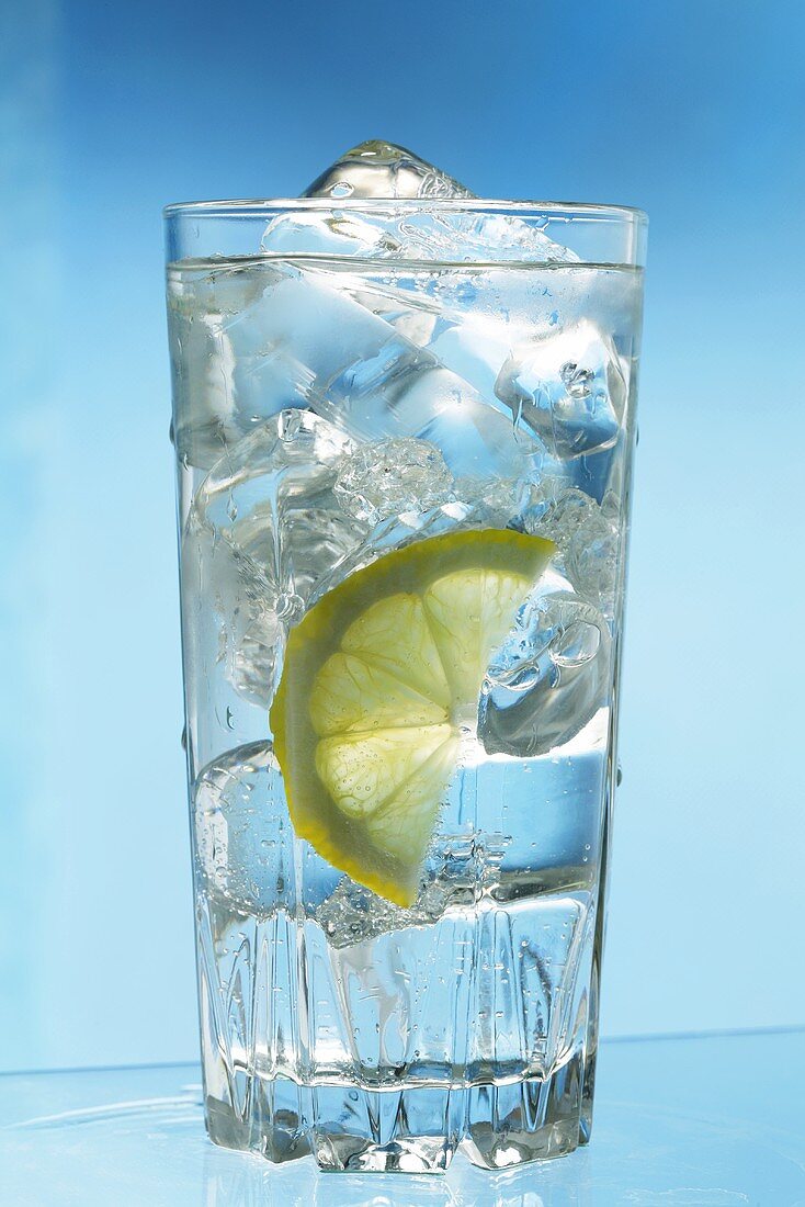 Ein Glas Wasser mit Eiswürfeln und Zitronenschnitzen