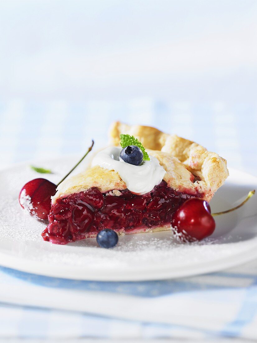A piece of cherry pie with fresh cherry and blueberries