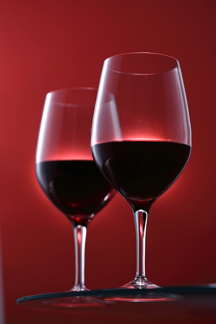 Two glasses of red wine against a red background