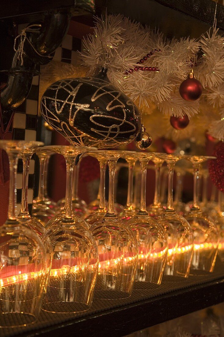 Empty, upside down wine glasses on the counter in a restaurant with Christmas decorations above