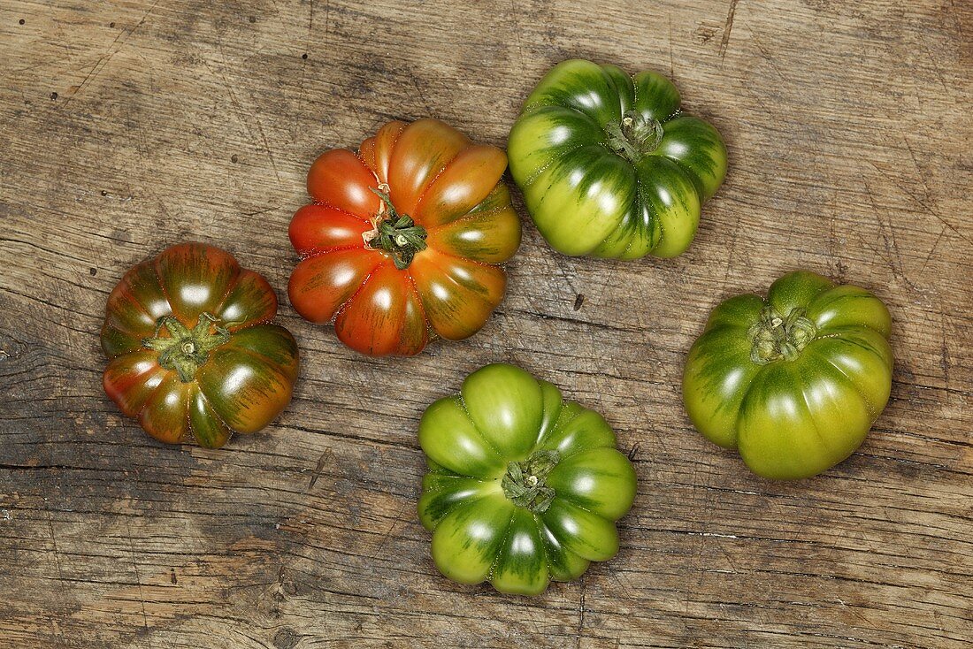 Red and green beefsteak tomatoes on a wooden surface