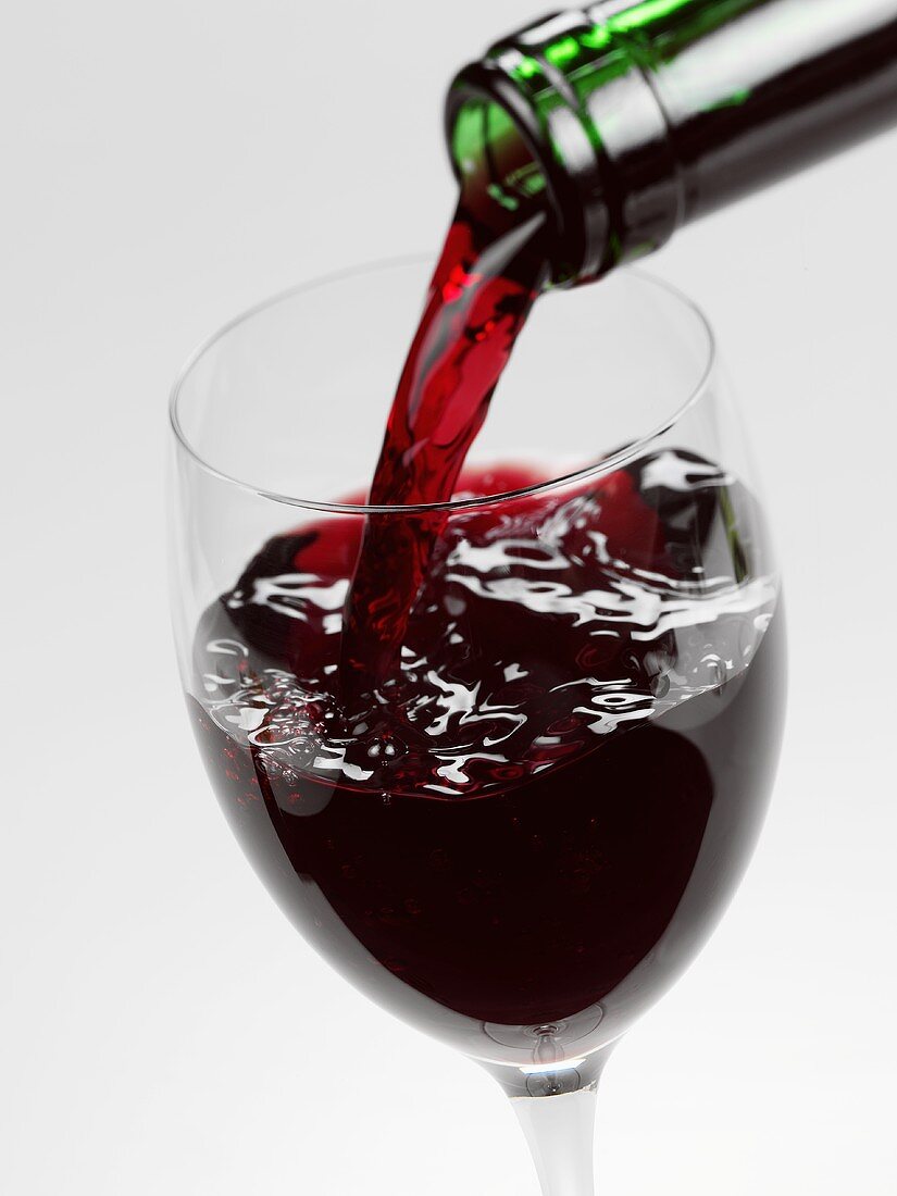 Red wine being poured into a half-full glass