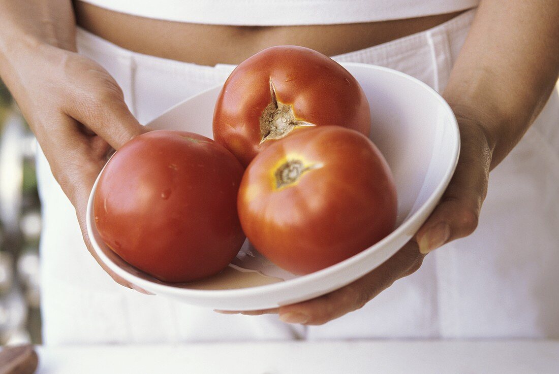 Young woman holding bowl with three tomatoes