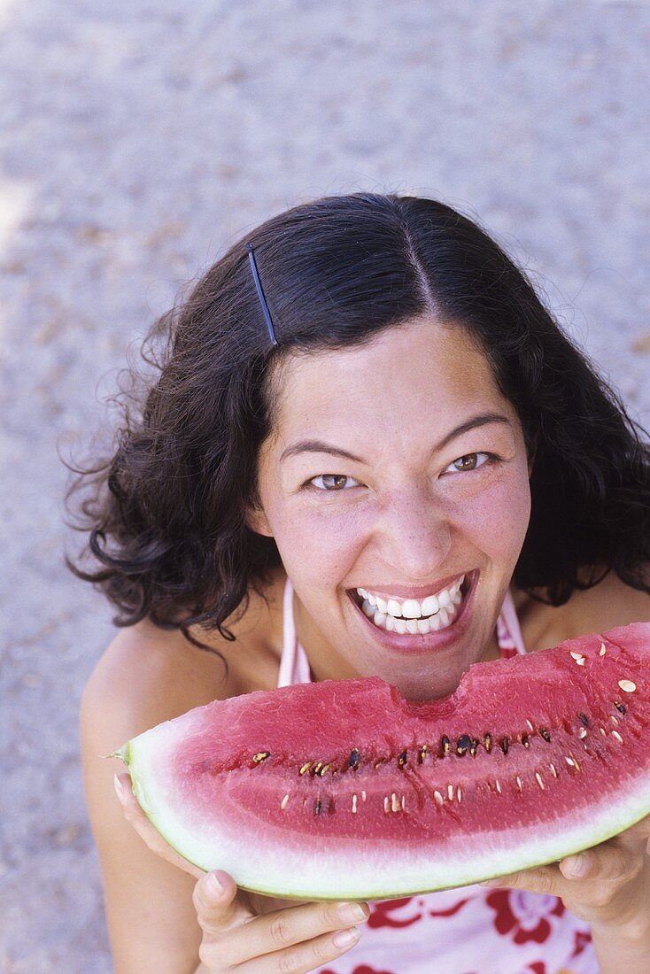 Young woman holding a wedge of watermelon with a bite taken