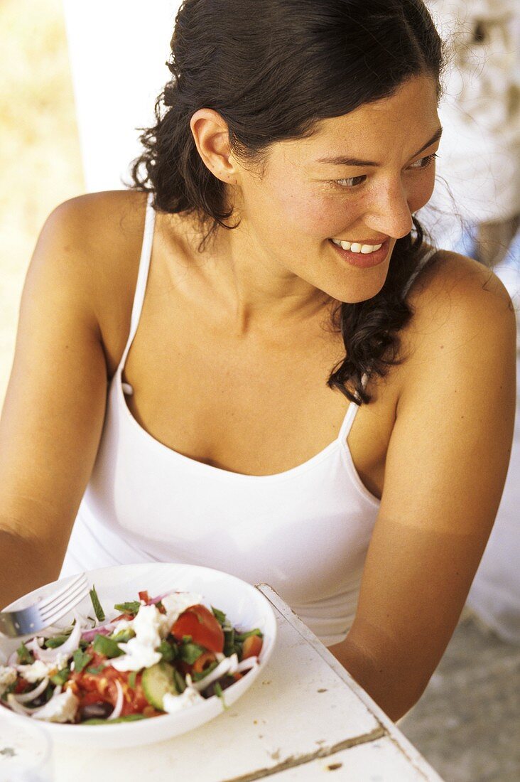 Junge Frau sitzt vor einem Teller griechischen Salat