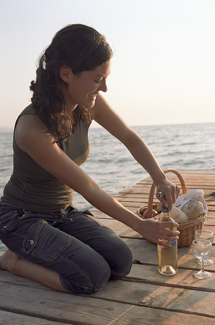 Junge Frau öffnet Weissweinflasche auf einem Steg