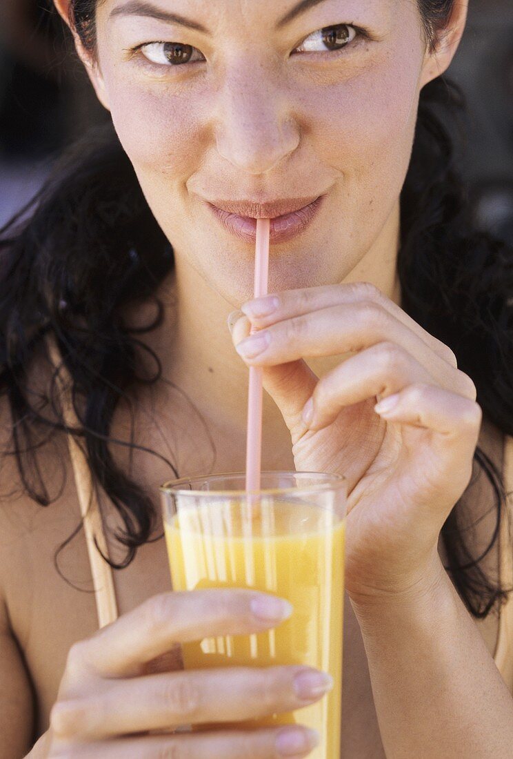 Junge Frau trinkt Orangensaft mit Strohhalm